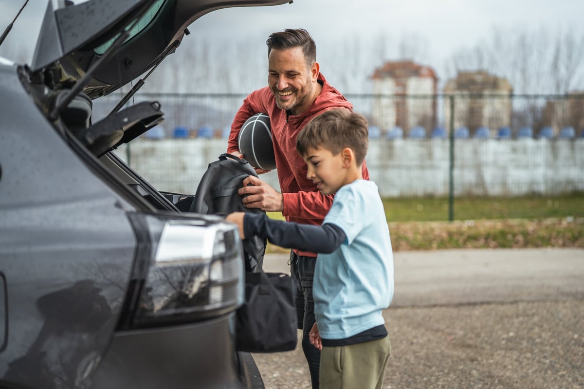Father and son packing sports bags and a basketball into a car trunk, preparing for outdoor training or a weekend game while bonding and sharing coaching moments together